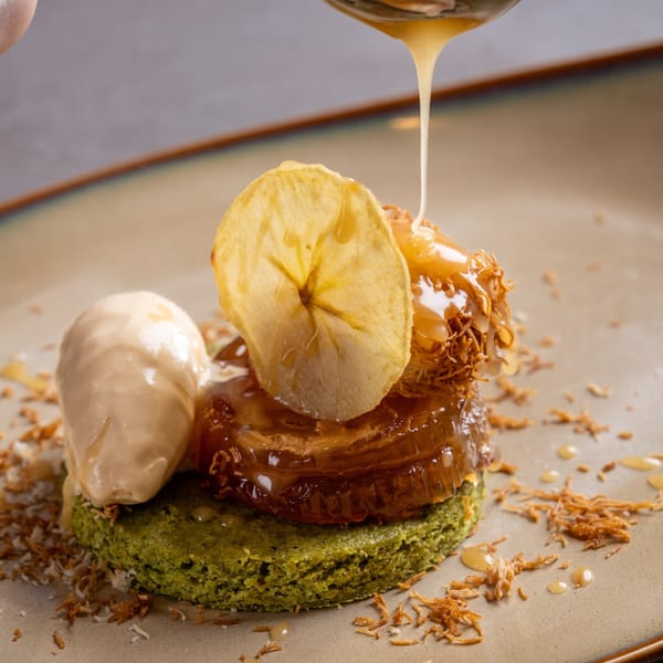 Caramel sauce drizzling onto a dessert with banana chips, ice cream, and green cake.