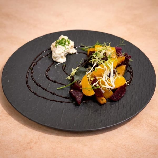 A black plate with a salad of beets, orange segments, greens, and a dollop of cheese.