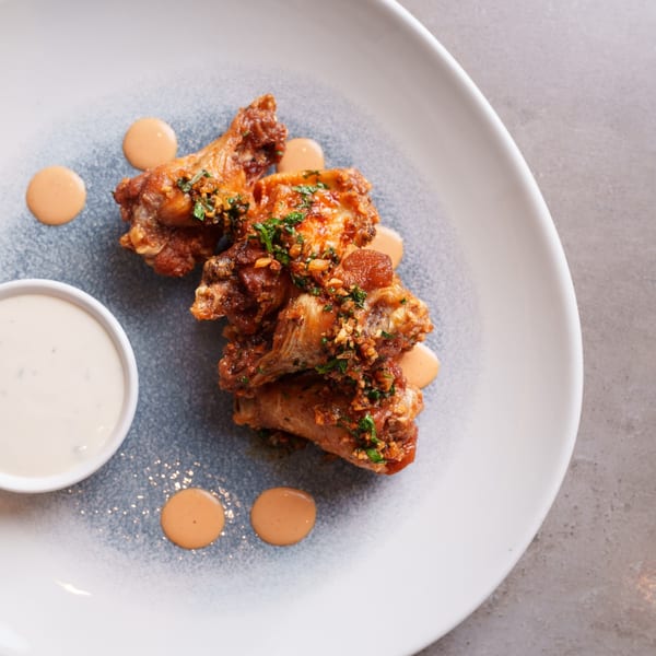 Crispy chicken wings with garlic and herbs, served with two dipping sauces on a speckled plate.