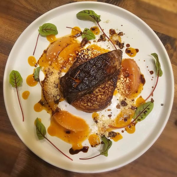 Seared foie gras on a bed of caramelized onions, drizzled with orange sauce and garnished with greens.