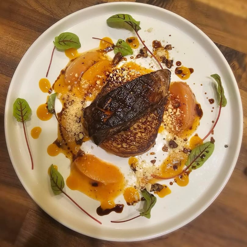 Seared foie gras on a bed of caramelized onions, drizzled with orange sauce and garnished with greens.